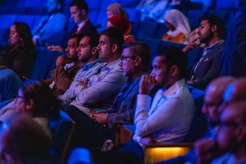 Attendees seated in the auditorium, lit blue, watching the main stage
